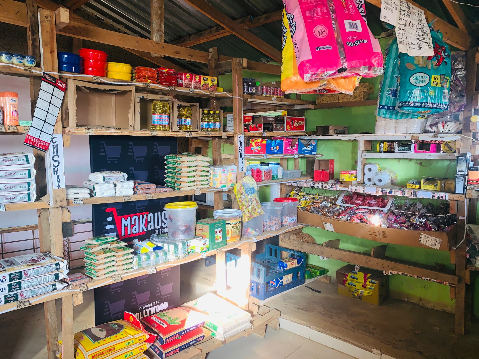 Inside Makausi Enterprise: wooden shelves stocked with maize meal, rice, cooking oil and snacks